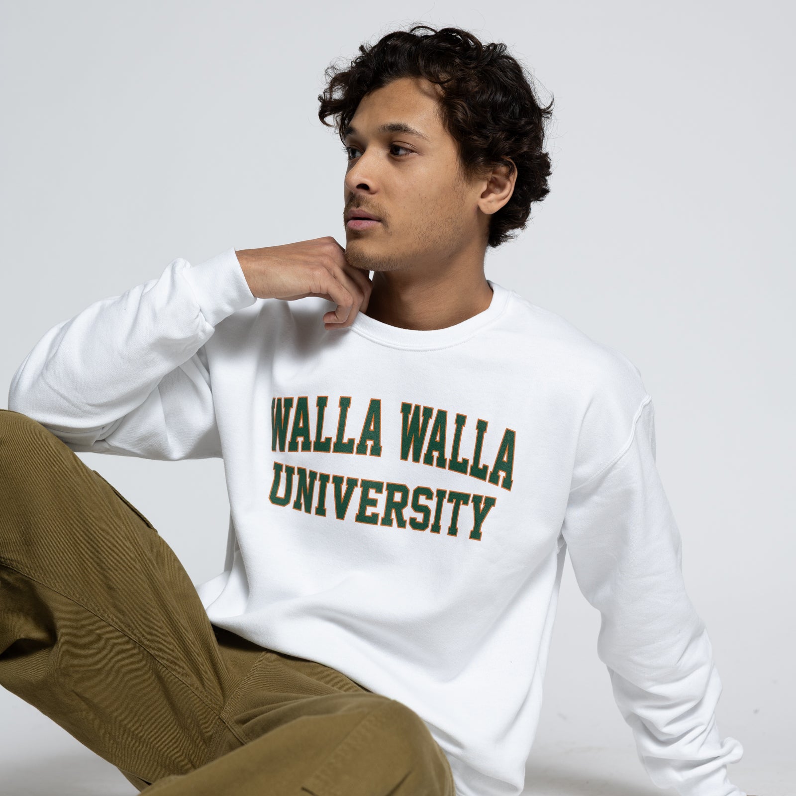 Man wearing a white sweatshirt with 'Walla Walla University' text, sitting on a white surface.