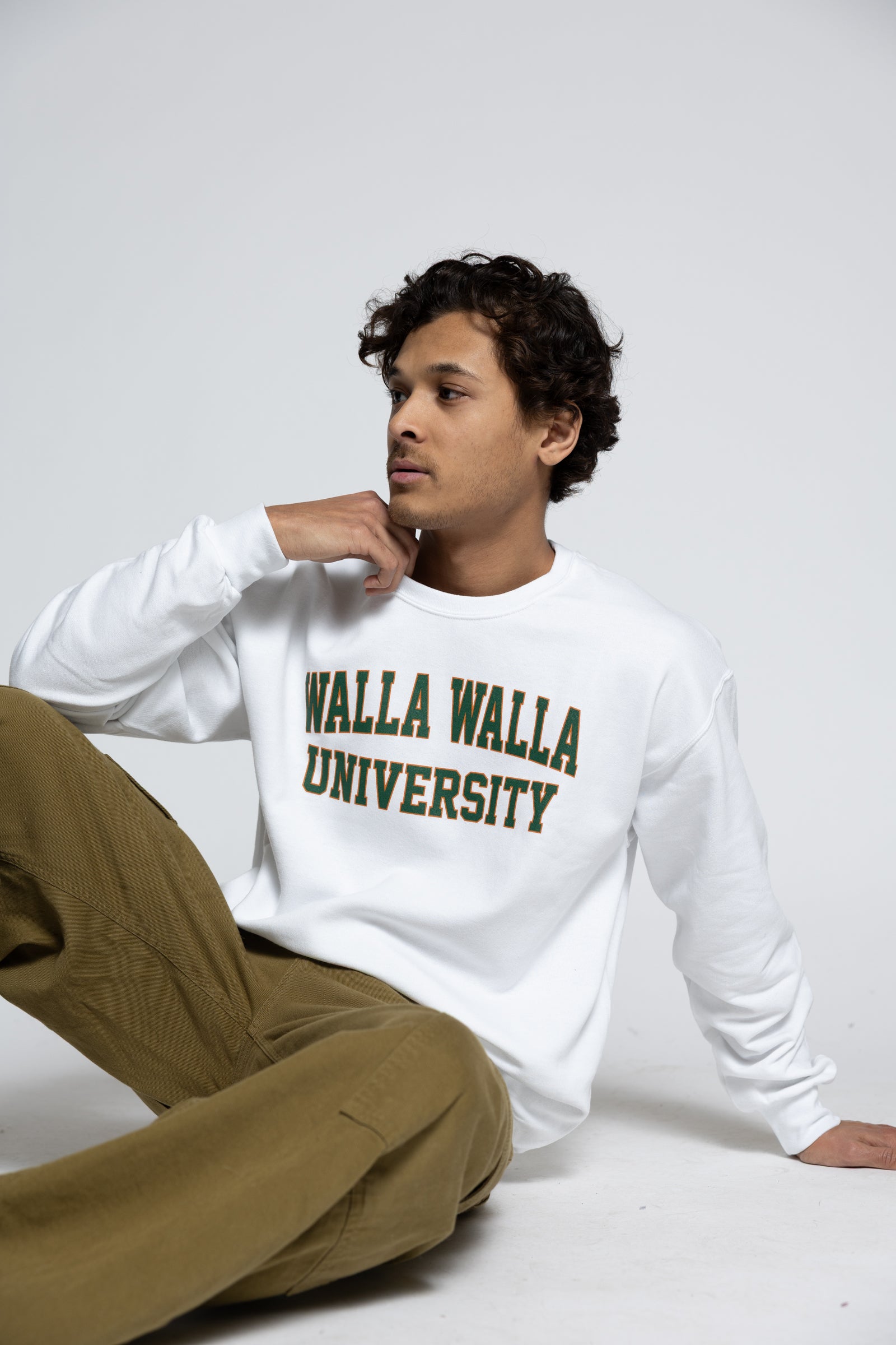 Man wearing a white sweatshirt with 'Walla Walla University' text, sitting on a white surface.