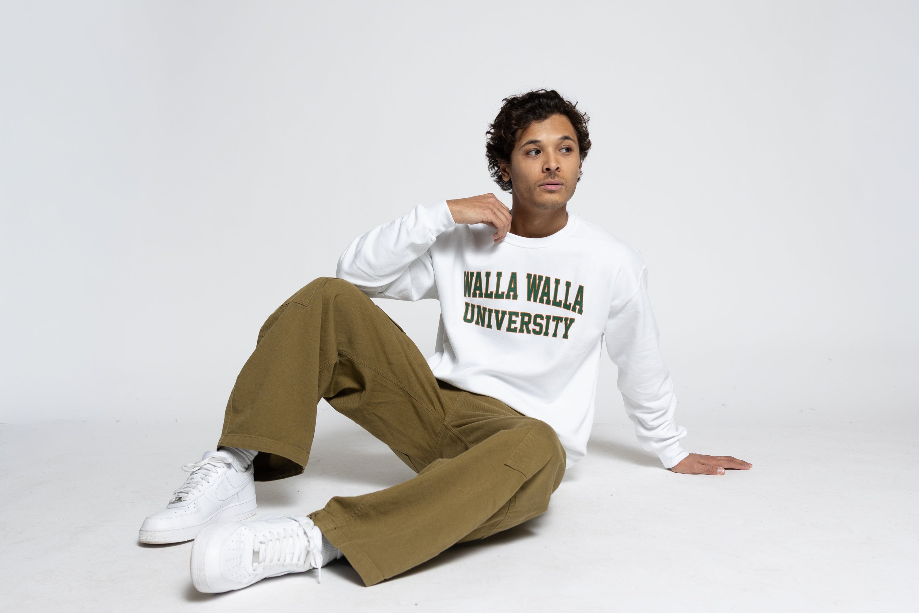 Man wearing a 'Walla Walla University' sweatshirt sitting on a white background